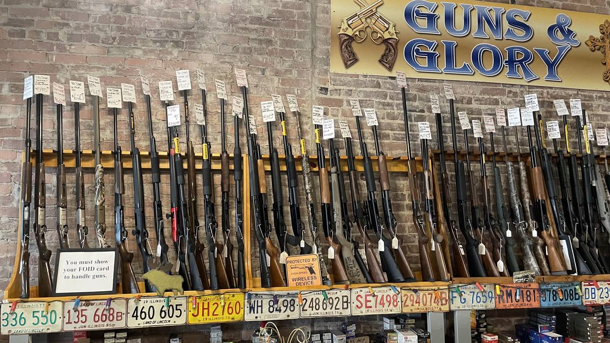 Wide shop wall under the Guns & Glory sign: TriStar Setter, Viper G2, Cobra III, Mossberg 500, 590, and Patriot, Weatherby SA-459, Remington 870, Henry rifles, Citadel, and Churchill, with vintage Illinois license plate trim along the bottom.