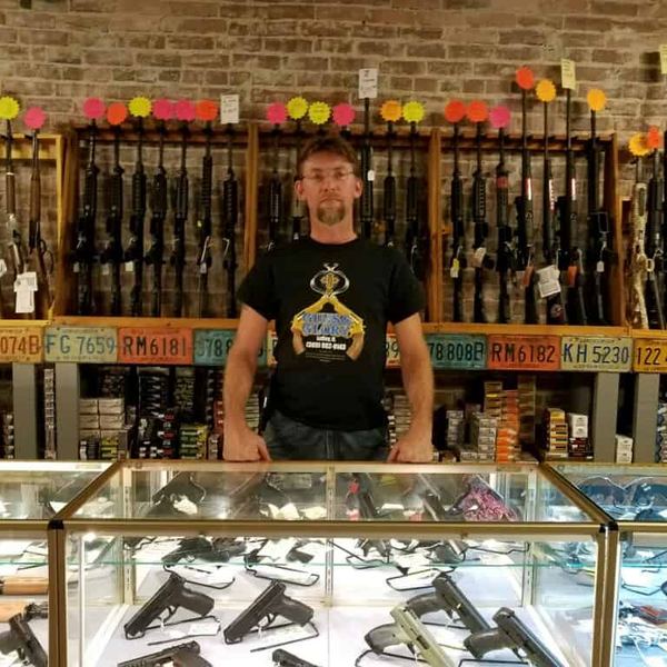 Matt Garvin, owner of Guns and Glory, standing behind the gun counter in front of the rifle wall and ammunition stock at the shop in Le Roy, Illinois.
